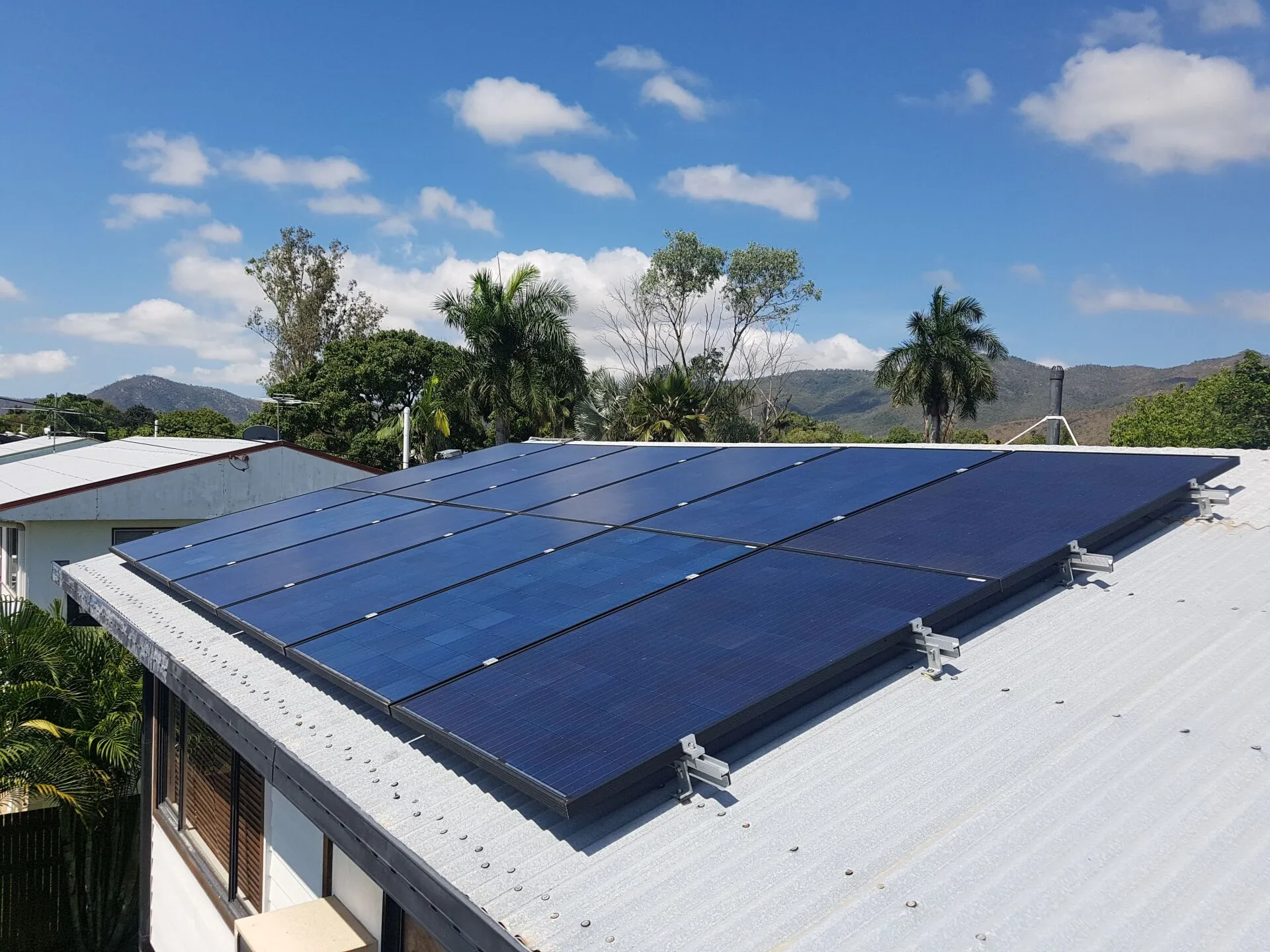 On Point Solar rooftop solar panel array on a Townsville home with palm trees and a mountain backdrop